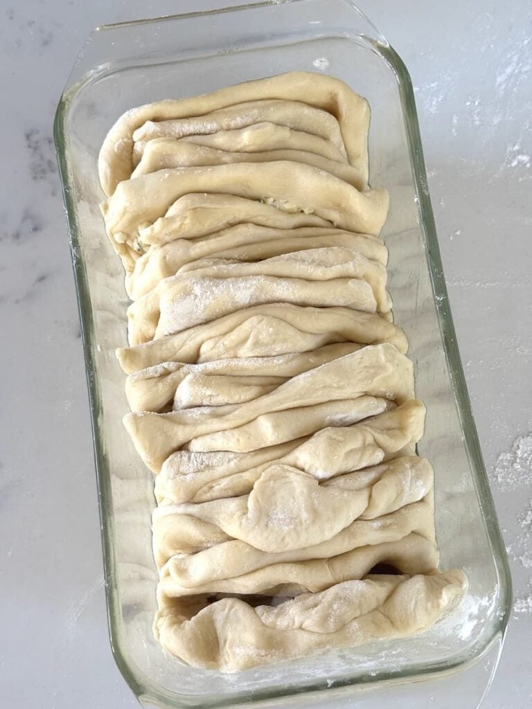 unbaked pull apart bread in greased glass loaf pan