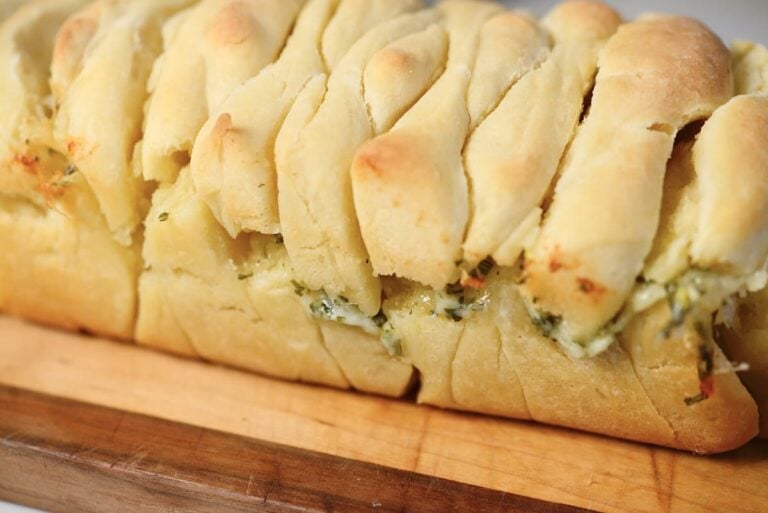 loaf of baked pull apart bread with herbs and cheese coming out on the sides