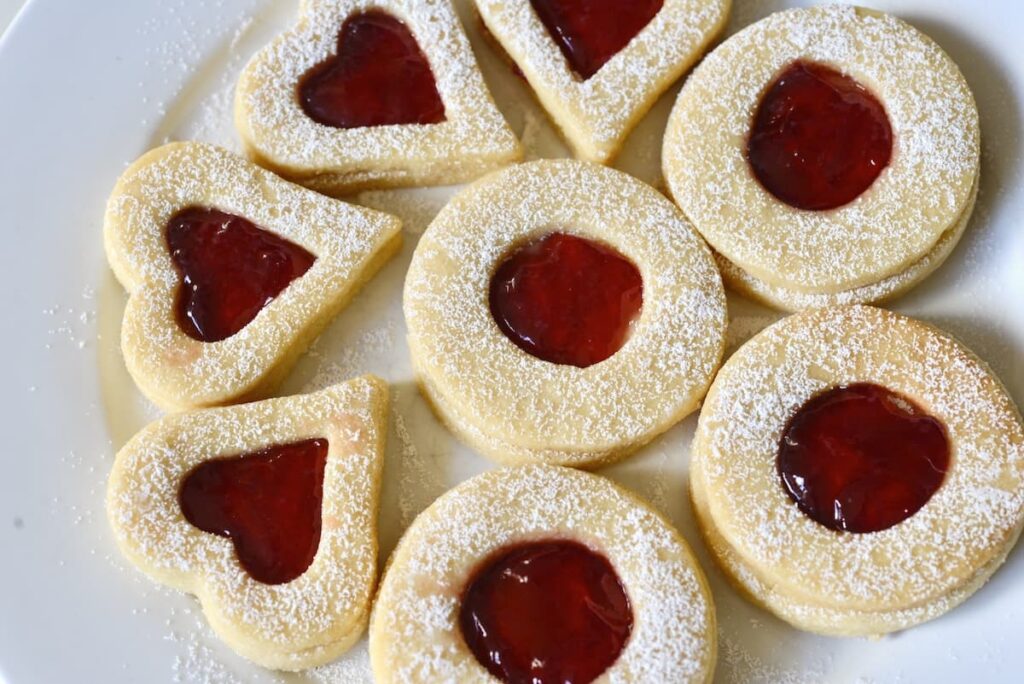 Linzer cookies dusted with powdered sugar on cookie plate