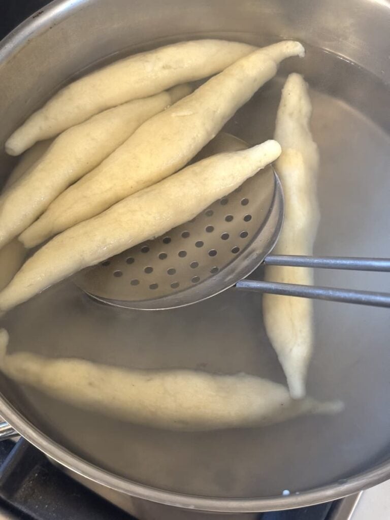German potato noodles cooking in water with slotted spoon