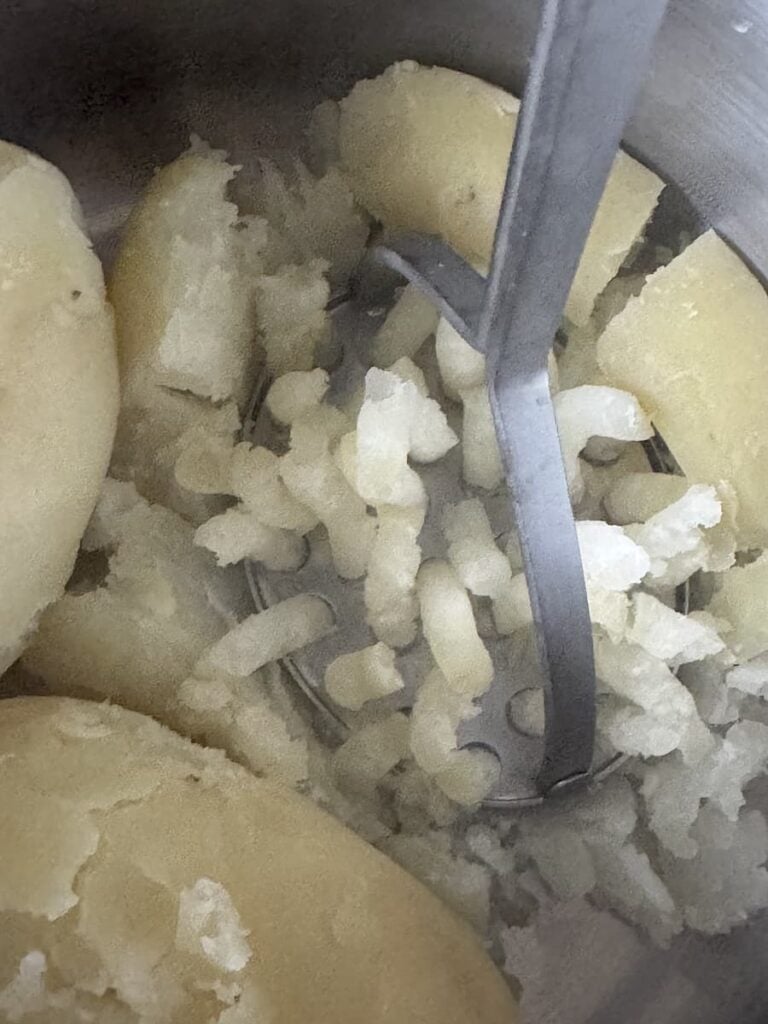 potato masher mashing cooked potatoes in pot