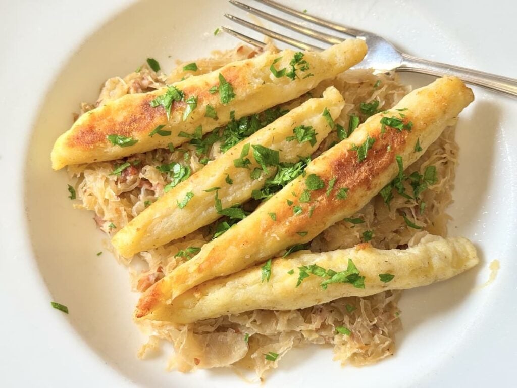 fried German potato noodles on plate over sauerkraut sprinkled with chopped chives
