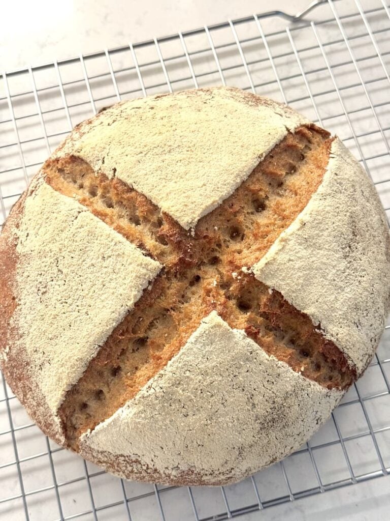 A round loaf of German Mischbrot with a dusting of flour and a large X-shaped score on top, cooling on a wire rack.
