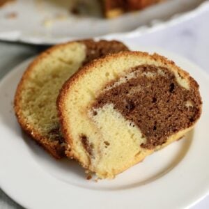 Two slices of marble cake, showing swirls of chocolate and vanilla, are served on a white plate with a silver fork beside them.