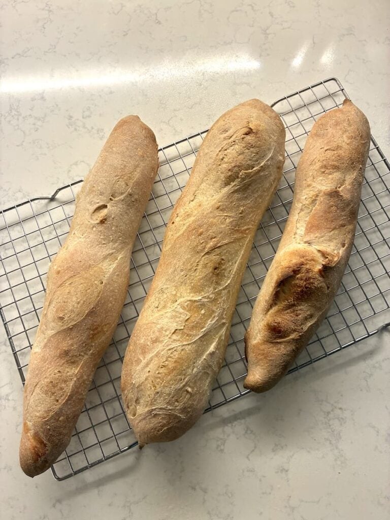 Three golden-brown sourdough baguettes cooling on a wire rack.