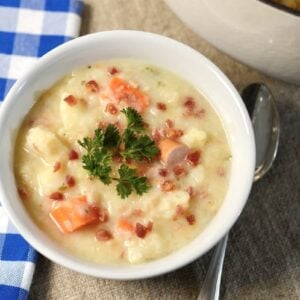 A bowl of creamy potato soup topped with bacon bits, sliced sausage, and parsley.