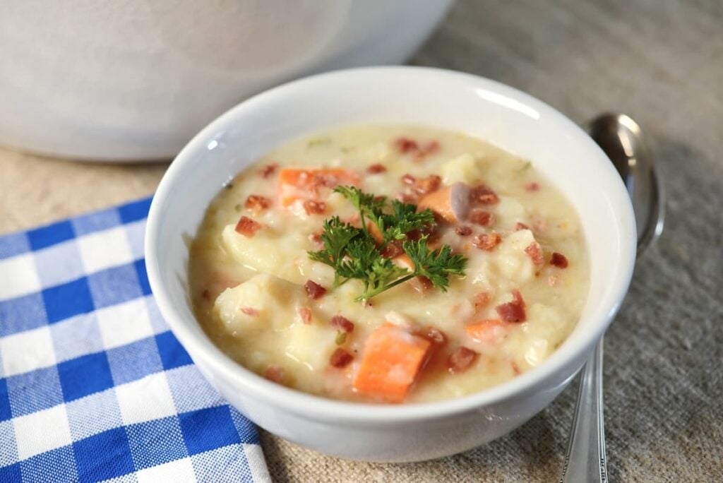 A bowl of creamy potato soup topped with bacon bits and a sprig of parsley.