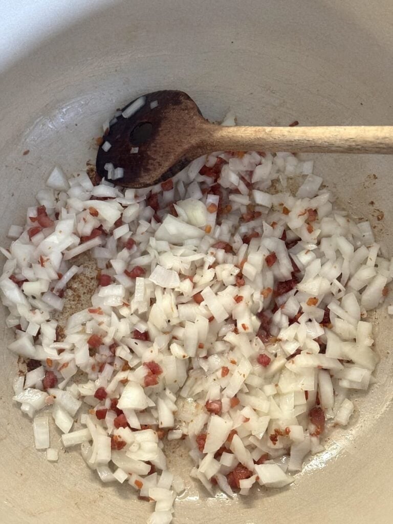Diced onions and bacon bits for potato soup sautéing in a pot with a wooden spoon.