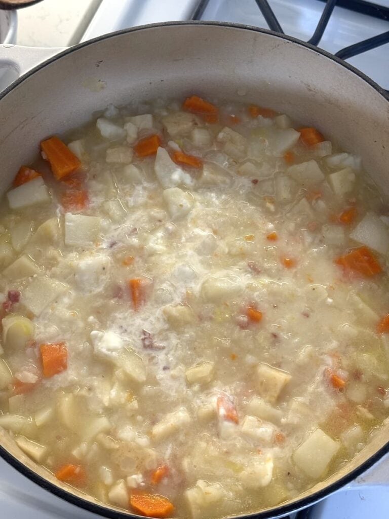 Creamy potato soup with diced carrots cooking in a pot on a stove.