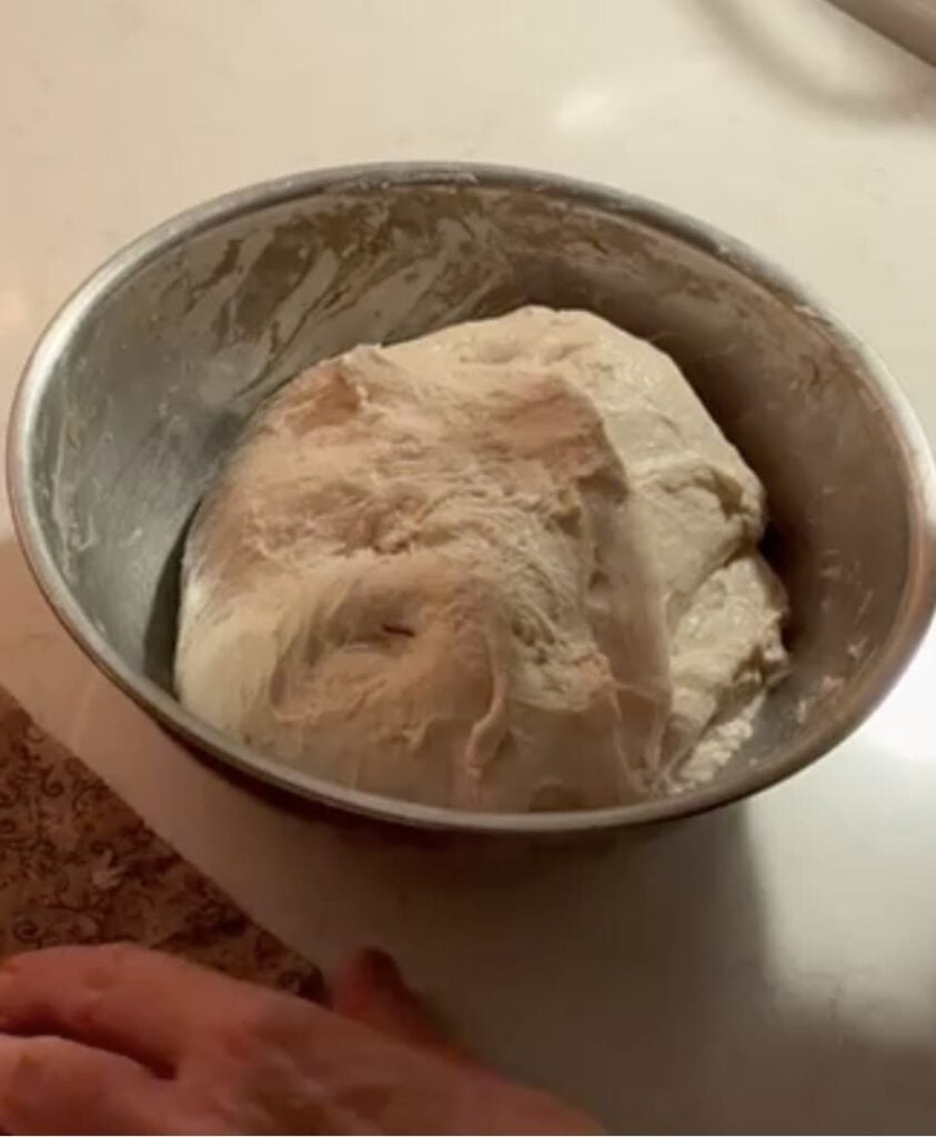A mound of raw sourdough baguette dough in a metal bowl.