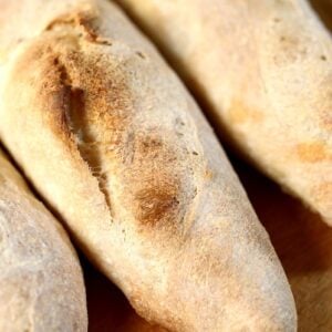 Three crusty, golden-brown sourdough baguettes on a wooden surface.