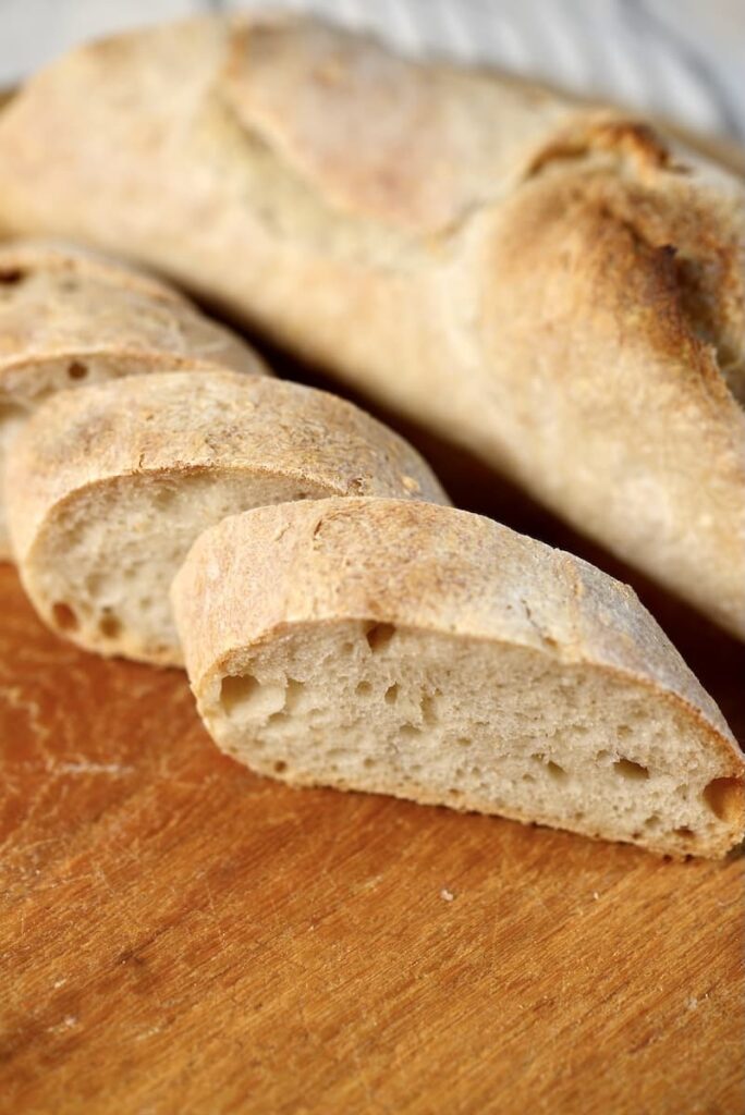 A sliced sourdough baguette on a wooden cutting board.