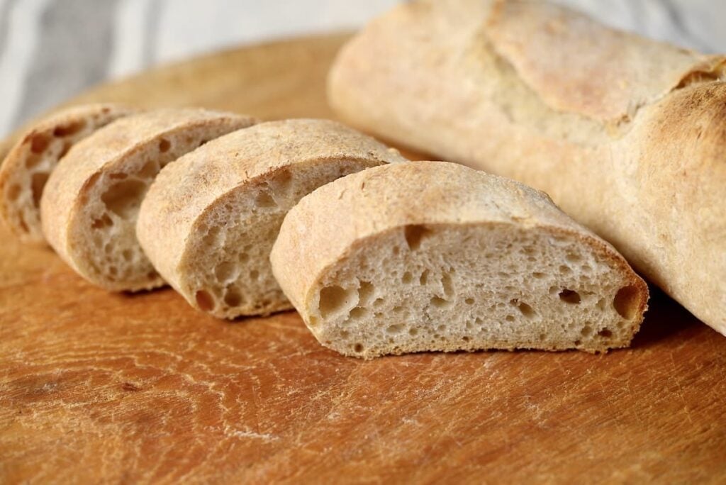 A crusty sourdough baguette partially sliced on a wooden cutting board.