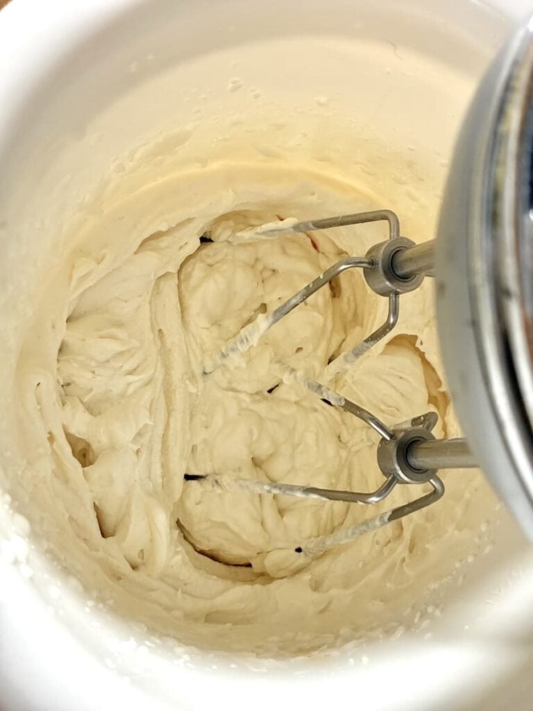 Electric hand mixer beaters mixing thick batter inside a white bowl.