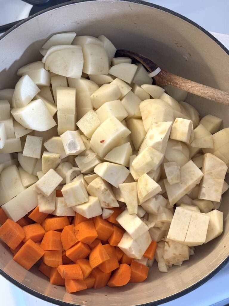 A pot of potato soup with chopped white root vegetables and diced carrots, with a wooden spoon resting on top.