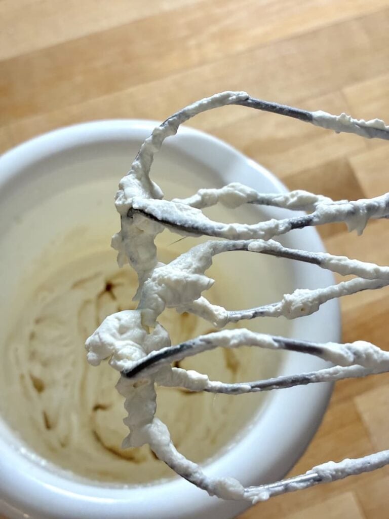 Handheld mixer beaters covered in whipped cream held over a mixing bowl.